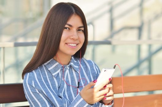 Young beautiful is asian girl sitts on the bench and listen to music. Spring sunny day