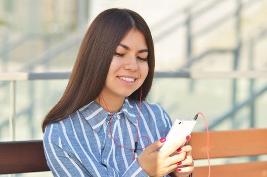 Young beautiful is asian girl sitts on the bench and listen to music. Spring sunny day