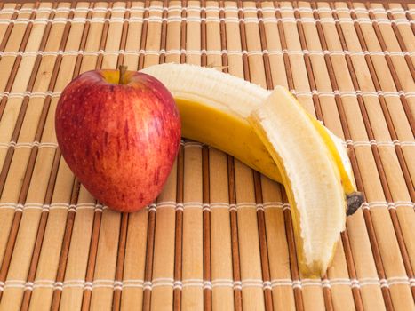 Side view of apple and peeled banana, on wooden slat table.