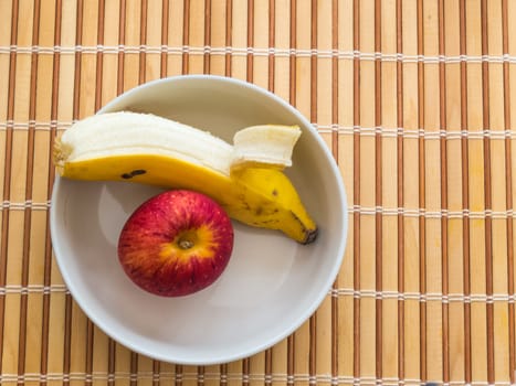 Healthy snack of banana and apple inside white bowl on wooden table.