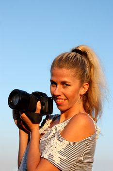 Blonde girl with camera. Smiling and looking in the camera.