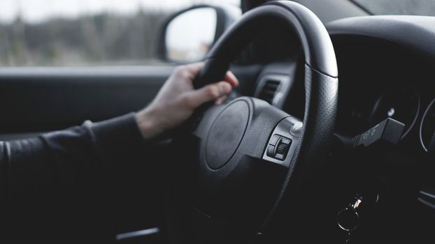 Interior view of car with black salon. Close-up Of A Man Hands Holding Steering Wheel While Driving Car