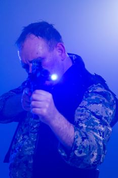 Soldier in army fatigues holding assault rifle in haze of blue smoke