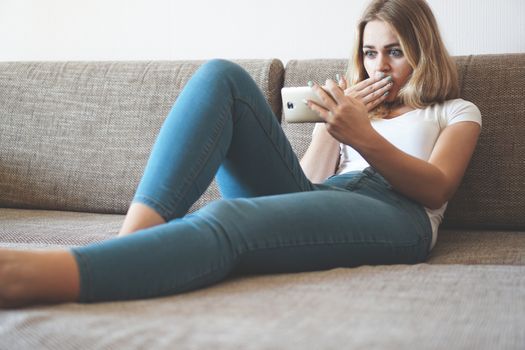 Shocked young woman looking at smartphone screen at home seeing something unbelievable on computer. Bad news concept, dismissal notice from boss