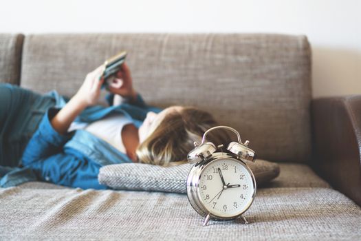 Young woman using phone in bed, looking at screen, insomnia, check time, wake up with smartphone, mobile phone addiction - alarm clock near