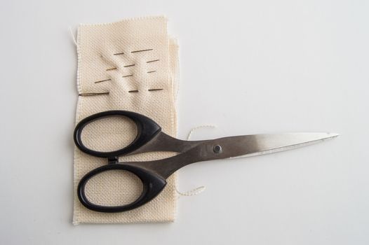 Sewing supplies SCISSORS, NEEDLE, fabric on white table, concept of minimalist, top, and accessories for handmade tailor.