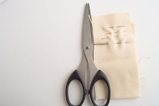 Sewing supplies SCISSORS, NEEDLE, fabric on white table, concept of minimalist, top, and accessories for handmade tailor.
