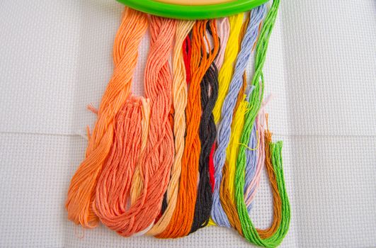 Bright colorful thread for embroidery thread on canvas. Handmade accessories on white background. Place for text, top view.