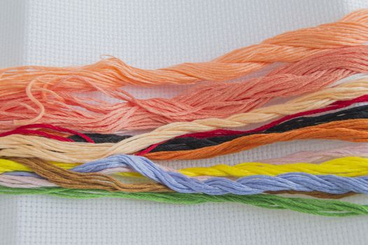 Bright colorful thread for embroidery thread on canvas. Handmade accessories on white background. Place for text, top view.