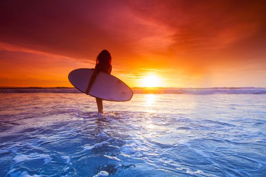 Beautiful surfer woman on the beach at sunset