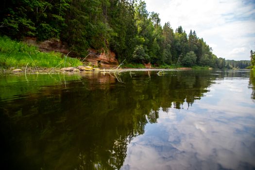 Landscape with cliff near the river Gauja and forest and clouds reflection in water. The Gauja is the longest river in Latvia, which is located only in the territory of Latvia. 

