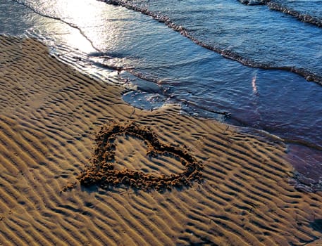 Drawing heart on the beach, small surf in sunny day.