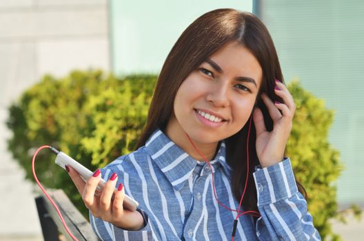 Young girl student holding a phone and listening to music on the street in the Park