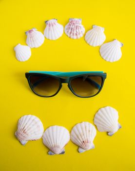 Semicircle of white seashells with sunglasses on yellow background like on vacation