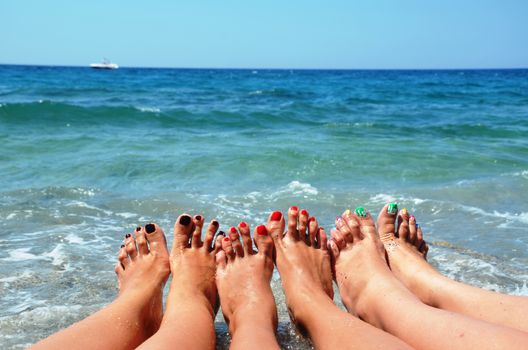 Close up of slender legs of three young girls. Blue sea in the background, the concept of a beach holiday.