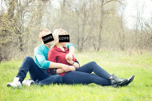 The couple is hugging on the green grass with the inscription on the face of the GDPR (General Data Protection Regulation)  ban on a photo of people on the street