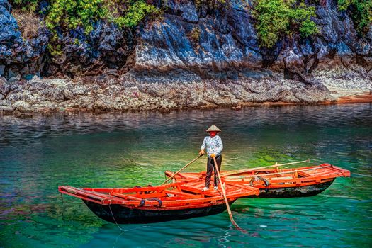 Unrecognizable vietnamese woman in conical hat rowing boats that bring tourists traveling inside limestone cave with limestone island in background in summer at Halong Bay. Quang Ninh, Vietnam.
