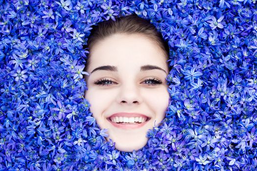 the girl is covered with blue spring flowers, the girl looks out from under the flowers. beautiful girl