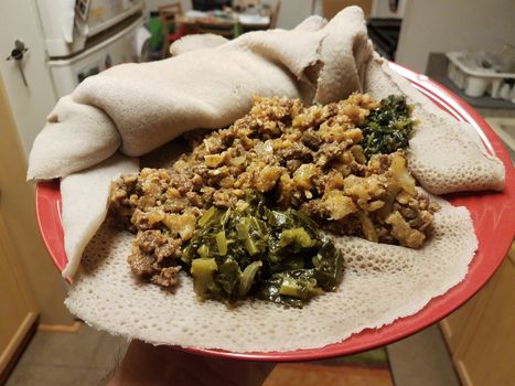 Ethiopian food beef and tripe with greens and bread on red plate in kitchen