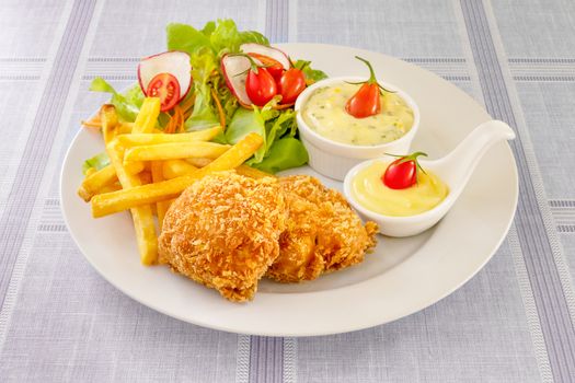 Deep fried fish steak served with french fries and fresh vegetables on white plate