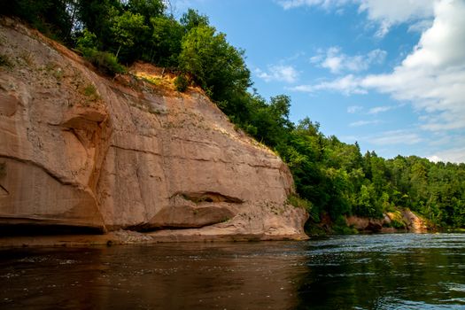 Landscape of cliff with cave near the river Gauja, blue sky and forest. Gauja is the longest river in Latvia, which is located only in the territory of Latvia. 