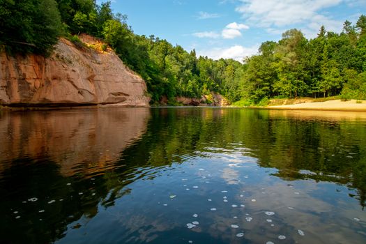 Landscape with cliff near the river Gauja, forest and clouds reflection in water. The Gauja is the longest river in Latvia, which is located only in the territory of Latvia.