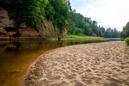 Landscape of cliff with cave near the river Gauja, sandy shore and forest in the background. The Gauja is the longest river in Latvia, which is located only in the territory of Latvia. 

