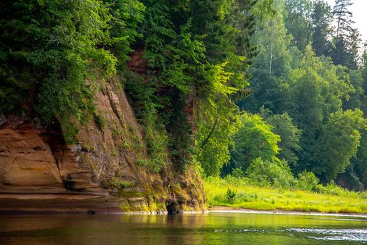 Landscape of cliff with cave near the river Gauja and forest in the background. The Gauja is the longest river in Latvia, which is located only in the territory of Latvia. 

