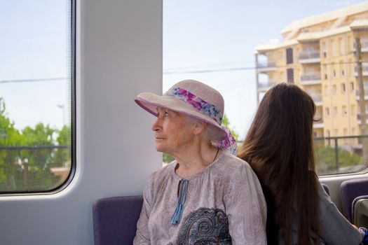 Beautiful gray-haired grandmother in a sunhat rides a commuter train and looks out the window.