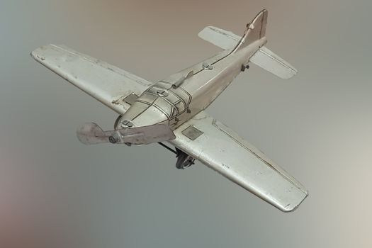 Picture of a retro gray metal toy airplane. In the background, blue sky with clouds and sea.