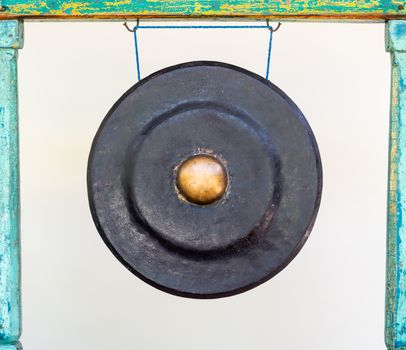 Black and golden traditional Asian gong attached to a green wood frame.