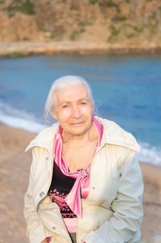 Portrait of the happy elderly woman against the sea in sunny spring day.