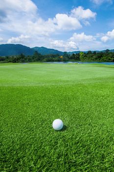 Golf ball above flag and green on tropical course in morning