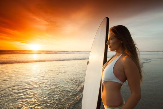 Beautiful surfer girl in bikini on the beach at sunset