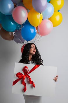 Young pretty woman with colored balloons and gift with ribbon bow or big greeting card