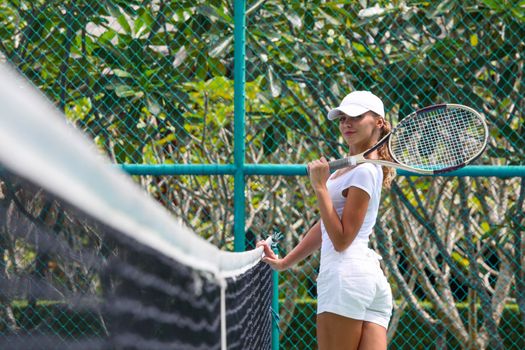 Female tennis player in white at tropical resort court