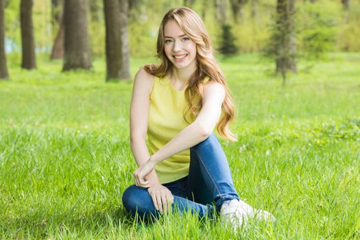 Pretty girl sitting on the grass in spring park and smiling