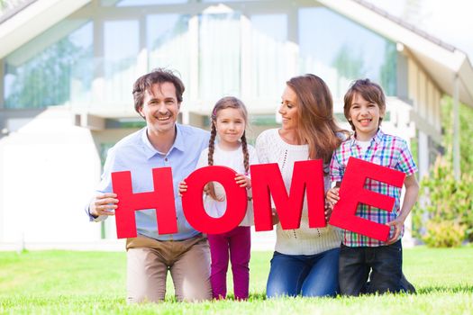 Happy family of parents and children in front of their house outdoors holding HOME letters