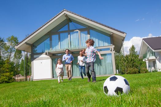 Family with children playing football on the backyard lawn near their house