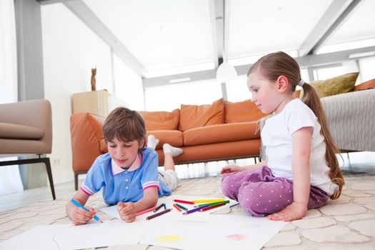 Little boy and girl drawing with color pencils on the floor playing together