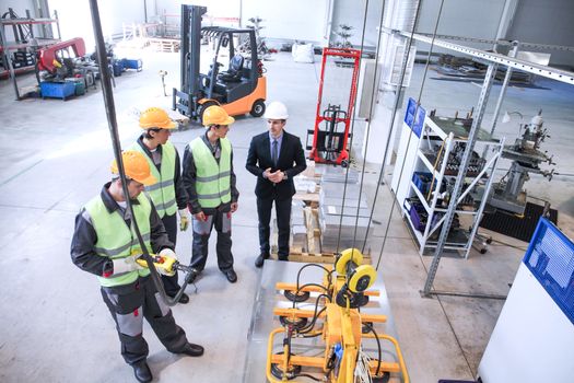 Manager and workers working with metal sheet lifting device at CNC factory