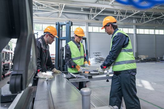 Team of three workers in CNC factory working at machine