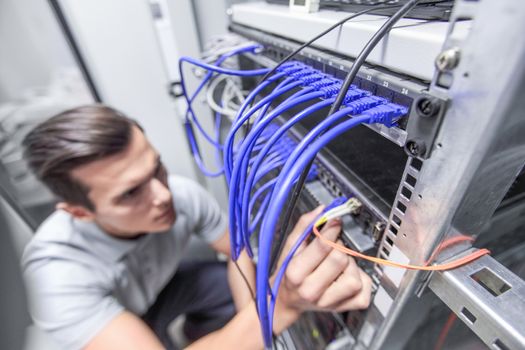 Young man working in network server room with fiber optic hub for digital communications and internet
