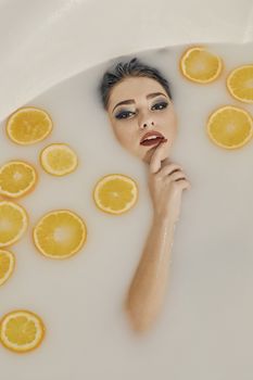 Young woman in the bath of milk and with oranges slices. Conceptual fashion photography for design. Skin care and a healthy lifestyle. Closeup naked young woman. Young woman for lifestyle design.