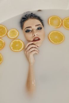 Young woman in the bath of milk and with oranges slices. Conceptual fashion photography for design. Skin care and a healthy lifestyle. Closeup naked young woman. Young woman for lifestyle design.