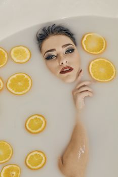 Young woman in the bath of milk and with oranges slices. Conceptual fashion photography for design. Skin care and a healthy lifestyle. Closeup naked young woman. Young woman for lifestyle design.