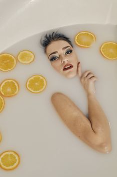 Young woman in the bath of milk and with oranges slices. Conceptual fashion photography for design. Skin care and a healthy lifestyle. Closeup naked young woman. Young woman for lifestyle design.