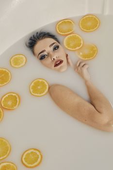 Young woman in the bath of milk and with oranges slices. Conceptual fashion photography for design. Skin care and a healthy lifestyle. Closeup naked young woman. Young woman for lifestyle design.