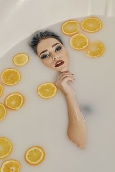 Young woman in the bath of milk and with oranges slices. Conceptual fashion photography for design. Skin care and a healthy lifestyle. Closeup naked young woman. Young woman for lifestyle design.