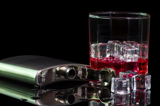 Stainless steel flask liquor alcohol and ice on table with red whiskey in glass on darkness background. Copy space for text or articles.